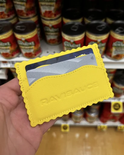 Hand holding the yellow ravioli card holder with RAVISAUCE embossed across the front